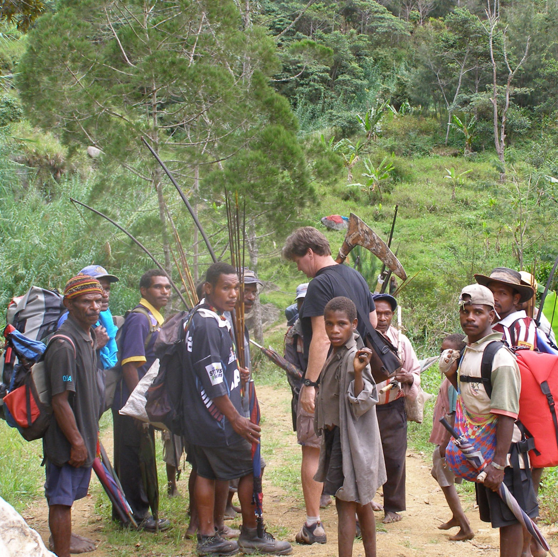 In the Kukukuku area, interesting region at the border of Eastern Highlands, Morobe and Gulf Provinces.  Looks like we are heading out of a village ready for the next.  I am holding quite a nice painting war club.  The bow and arrows the other men are holding are for protection and hunting while on the trail—not things I purchased—circa 2006/7.